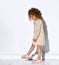 Side view of little adorable girl with curly golden hair looking down admiring her new fashionable sandals.