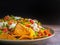 Side view of loaded minced pork nachos on plate with black wall background