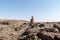 Side view of a lone stone man sitting on a rock, appearing be be just resting next to the road. These lone men are a mystery found