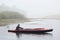 Side view of male kayaking on river, sportsman in black jacket looking at foggy water, holds oar in hands, foggy day, man in boat