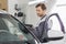 Side view of male maintenance engineer holding tablet PC while examining car in workshop