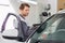 Side view of male maintenance engineer holding tablet PC while examining car in workshop