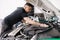 Side view of a male mechanic working in his garage. Young bearded man checks the engine in the car, the hood is open