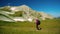 Side view of male tourist walking on grass with backpack and trekking near beautiful small chalk mountain. Woman enjoys