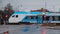 Side view of modern electric passenger train during cold winter rain is rushing through a grade crossing with road with barriers