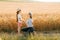 side view of mother and daughter in hat holding hands in golden wheat field.