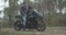 Side view of motorcyclist sitting on black motorbike as smiling woman coming and talking. Wide shot of positive young