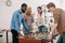 side view of multicultural businessmen playing table football and female coworker pointing