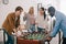 side view of multicultural businessmen playing table football in front of female