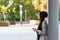 Side view of a muslim adult woman leaning on a support beam column looking forward while using her phone