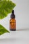Side view of Natural essential oil, serum glass drop bottle on a gray background wit green leaves. Alternative medicine, aromatic