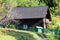 Side view of newly built small dark brown mountain wooden log cabin surrounded with green metal fence and forest vegetation