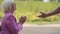 Side view of a nice blonde mature woman sitting in the summer park and clapping her hands. Male senior hand appearing