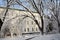 A side view of Nizhyn Gogol State University white historic old building through winter snow covered trees. A winter walkway to