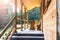 Side view of an open veranda in front of a wooden forest cottage. Pine forest under the sun rays in the background.