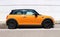 Side view of an orange Mini Cooper, or Mini Hatch, parked on the roadside.