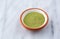 Side view of organic powdered wheat grass in a small bowl on a gray marble counter top