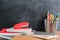 Side view over a wooden desk with school supplies on it. Bucket with colored pencils, notebooks, rulers, stepler. Back to school c