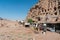 Side view photograph tourist stands in front of of the Royal Tombs and facades at Petra, Jordan