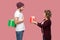 Side view portrait of amazing couple of friends in casual style standing, girl giving present box, boy hide behind gift, celebrate