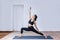 Side view portrait of brunette young woman wearing sport clothes working out against white wall, doing yoga or pilates exercise.