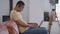 Side view portrait of concentrated young African American man in earphones typing on laptop keyboard sitting on couch in