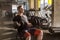 Side view portrait of concentration young adult man handsome athlete working out in gym, sitting on a bench and holding two