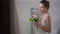 Side view portrait of confident beautiful proud young bride in wedding dress standing with bouquet in bathroom at home