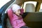 Side view portrait of cute girl in pink jacket and beautiful hat sitting in car. Concept of smiling little girl resting in car