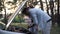 Side view portrait of focused man leaning at open car hood talking with woman standing at background. Worried Caucasian