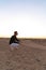 Side view portrait of handsome young man in black shirt and white pants that crouched among the desert and looking