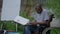 Side view portrait of paraplegic African American man in wheelchair outdoors examining paperwork. Concentrated serious