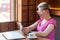 Side view portrait of shocked screaming young blogger with blonde short hair in pink t-shirt is sitting in cafe, holding phone