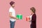 Side view portrait of suprised couple of friends in casual style standing, giving present boxes to each other, celebrate