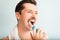 Side view portrait of young man with towel on shoulders brushing white teeth with modern electric toothbrush, close-up.