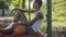 Side view of positive African American sportsman sitting with ball on basketball court and listening to music in