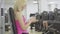 Side view of positive blond woman typing on smartphone with men training at the background. Portrait of young beautiful