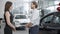 Side view of positive man and woman talking in car dealership and shaking hands. Handshake of happy buyer and