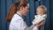 Side view positive pediatrician talking to baby girl cheering up little child. Beautiful Caucasian woman calming down