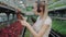 Side view of positive young Caucasian woman in headphones dancing as checking plants in greenhouse. Portrait of slim