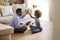 Side view of pre-teen girl sitting cross legged on the floor of the sitting room giving a high five to her grandfather after build