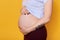 Side view of pregnant female with belly isolated over yellow background. Woman with tattoo on hend dressed casually being