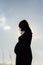 Side view of pregnant woman posing at sunset. Pregnant woman touching gently her tummy.