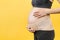 Side view of pregnant woman wearing elastic maternity band at yellow background with copy space. Close up of orthopedic abdominal