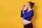 Side view of pretty pregnant lady eats fast food, wearing blue shirt and leggins, with bunch on head, poses in studio while biting