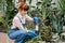 Side view of pretty smiling girl in jeans overalls and gloves, in the process of planting succulent in little black pot