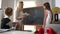 Side view professional teacher and curios student standing at chalkboard in classroom talking. Caucasian woman asking