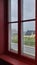 Side view of a red wooden window with double glazing. Rainy outdoor landscape. Background sea and gray sky.