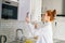 Side view of redhead young woman opening door of kitchen cabinet at light modern kitchen room.