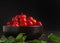 Side view of ripe red acerola cherries fruit in a ceramic bowl with a black background.